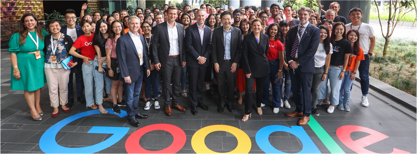 Large group of people stand over a Google logo on the ground.
